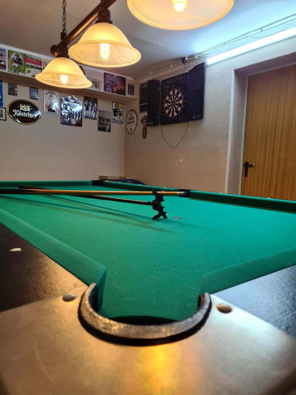 Billardtisch mit Queues, dahinter eine Dartscheibe an der Wand