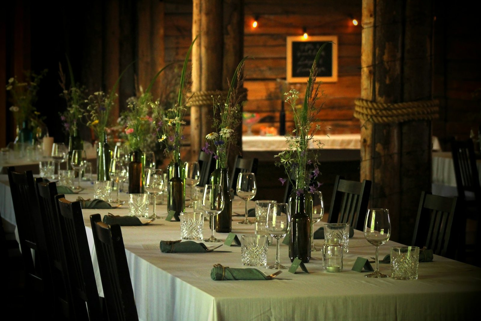 Lange festlich gedeckte Tafel mit Wildblumen, Weingläsern und Stoffservietten, vorbereitet für eine private Feier